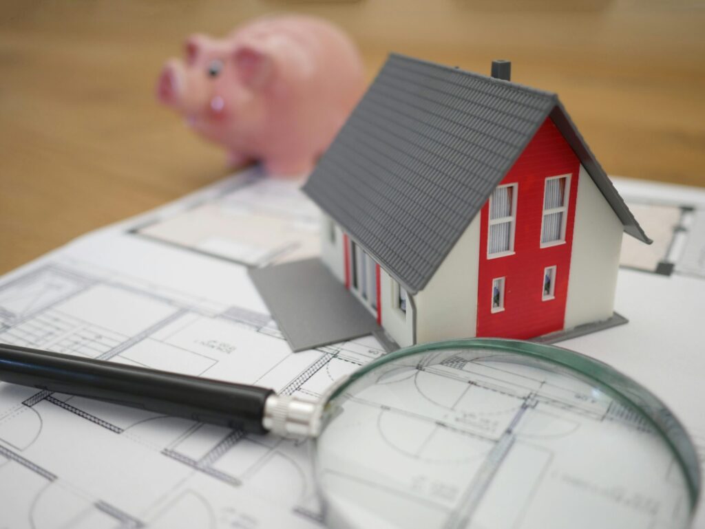 white and red miniature house and magnifying glass on top of a floor plan